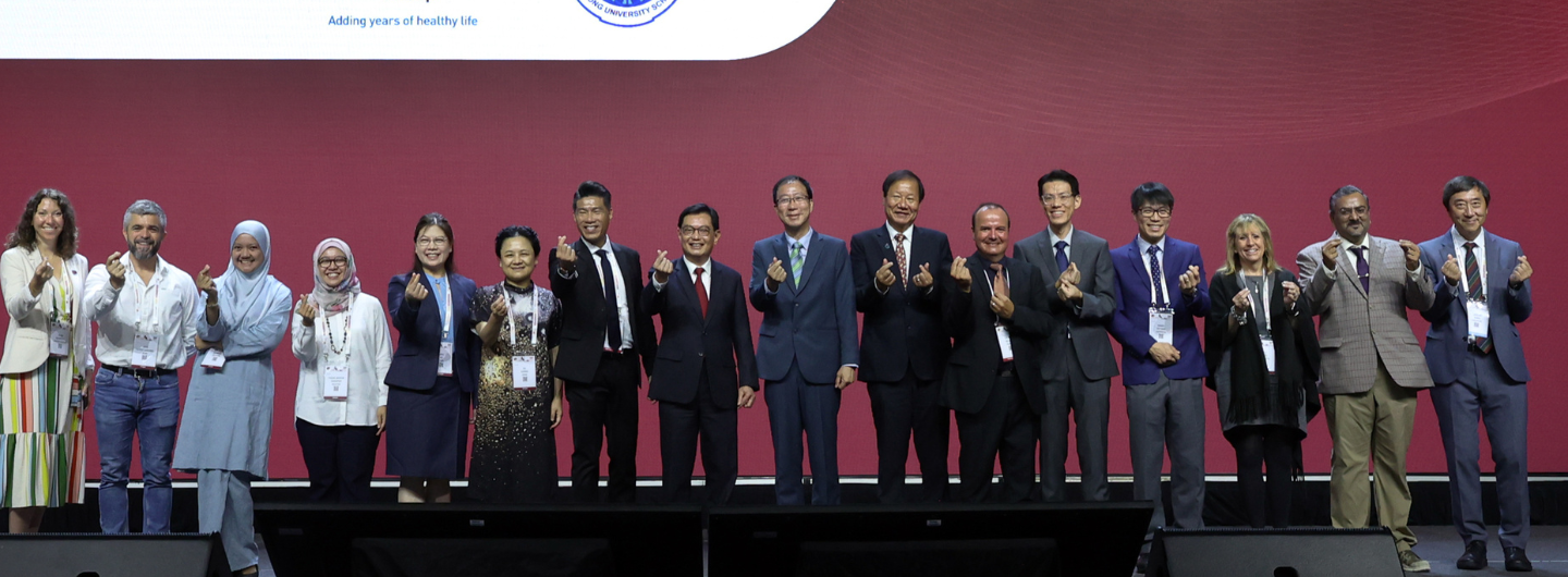 Group of people making heart gestures with their hands on a stage with red backdrop.